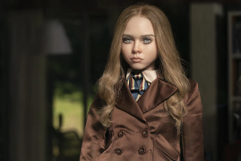M3gan the doll has long well placed hair and wears a trench coat.