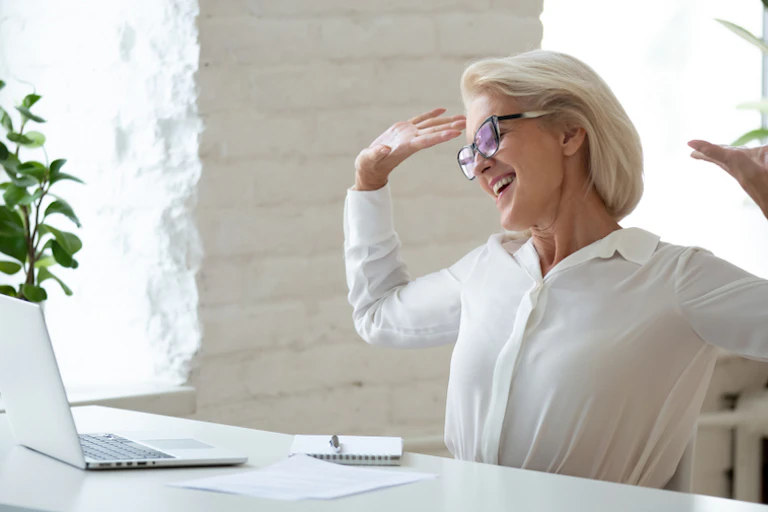 Smiling mature female boss or office worker stretching arms enjoy working day ends