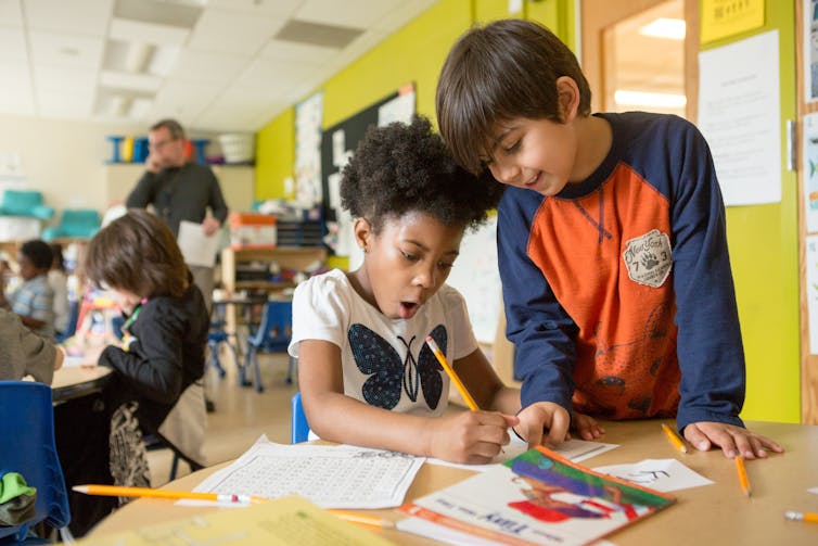 Two children discussing something in a classroom.