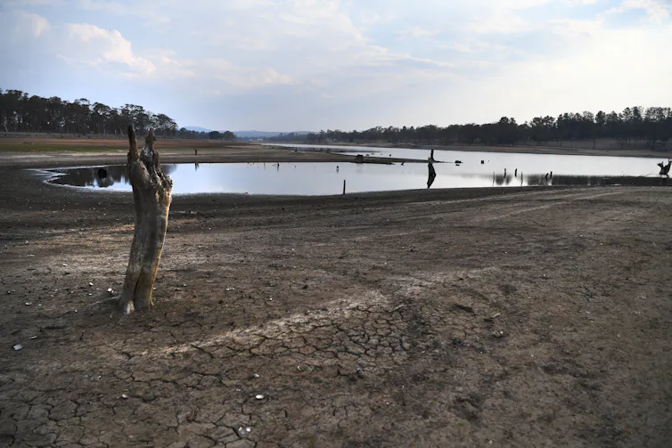 Cracked dry mud around dam water that's down to very low levels
