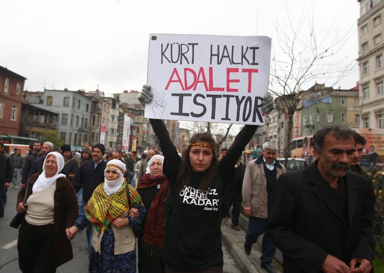 women wearing hijabs and carrying a sign reading KURT HALKI ADALET ISTIYOR.