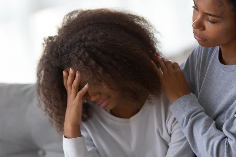 A woman comforts an adolescent who has her head in her hands and looks upset