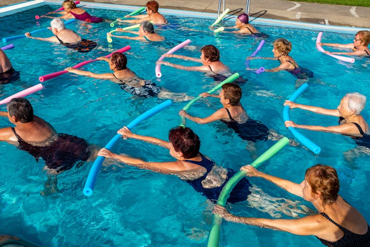 A group of elderly women do water aerobics in an indoor pool.
