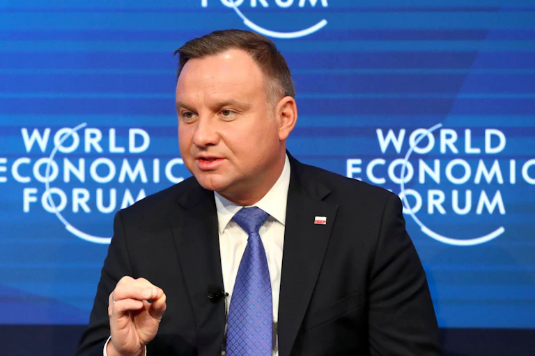 A man with a blue tie in front of a banner saying World Economic Forum.