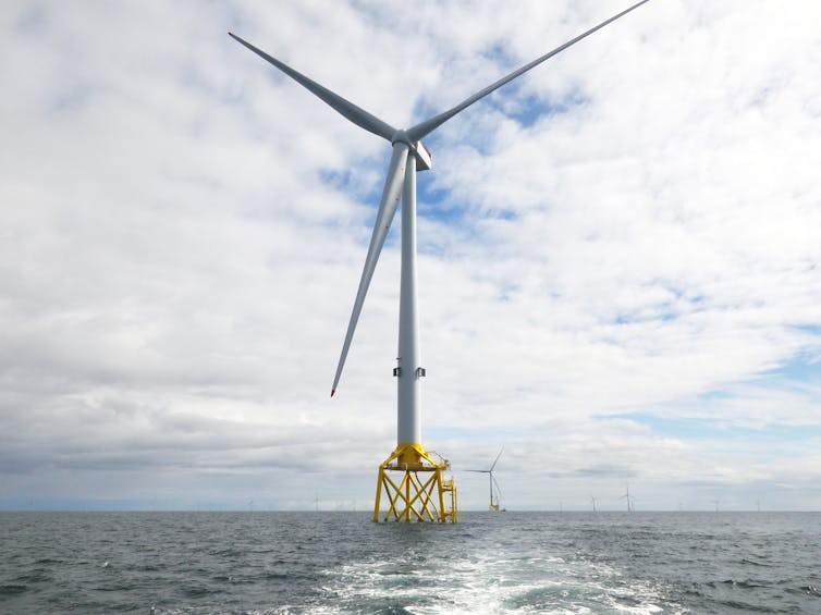 A wind turbine on a yellow platform in the ocean.