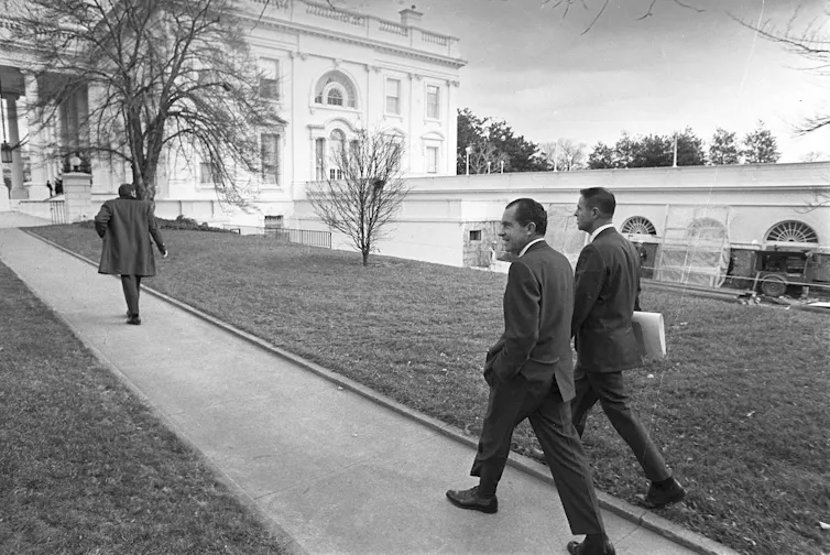 Two men in suits walking on a path toward the White House.