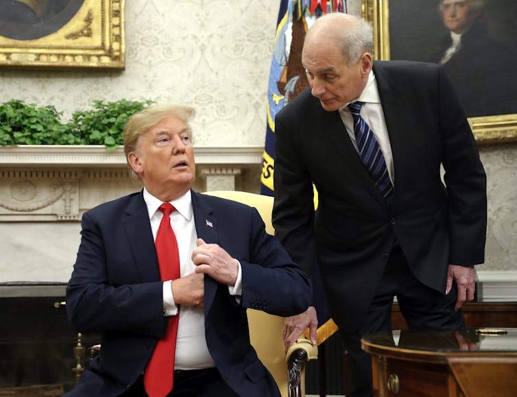 Two men in suits, one with a bright red tie, in an elegant room.