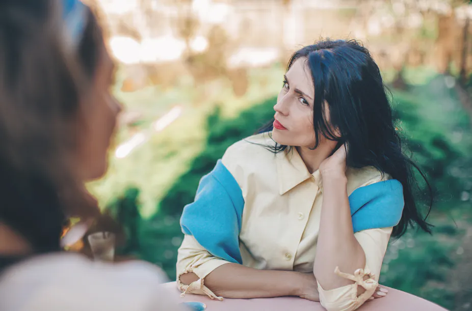 Woman with an indignant expression looks at her friend sitting at a round table in a cafe,
