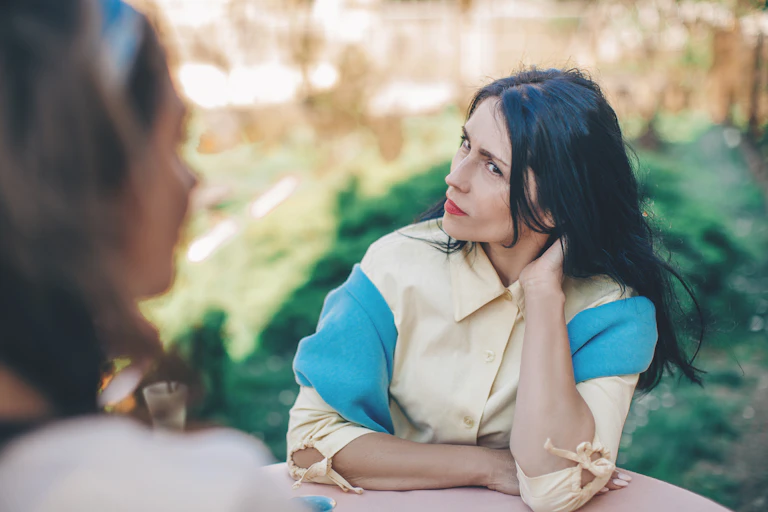 Woman with an indignant expression looks at her friend sitting at a round table in a cafe,