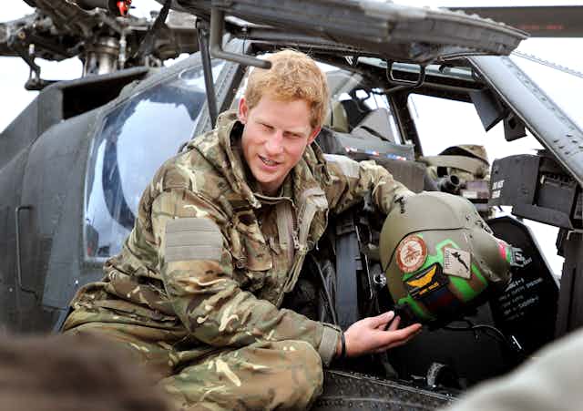 Close-up of a man dressed in military uniform sitting near a military helicopter.