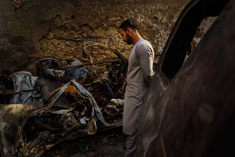 A man wearing white clothes looking at scattered clothes and other belongings.
