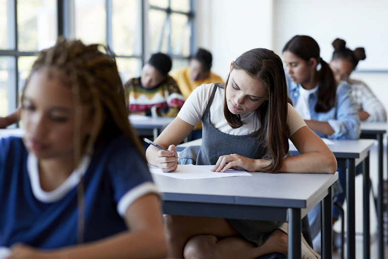 Students sit at desks writing on papers