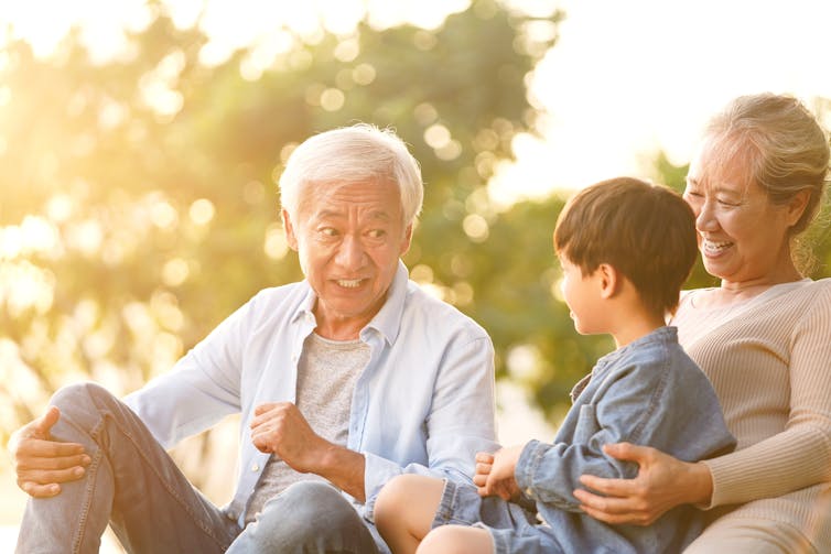 An elderly Asian man speaking to a younger boy who is sitting in a woman's arms.