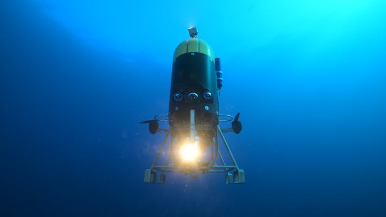 A large robot with a light and sensors descends into darker water