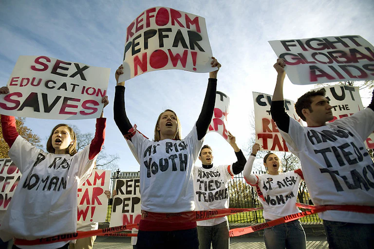 Protestors holding up signs reading "Sex education saves," "Reform PEPFAR now!" and "Fight global AIDS" among others