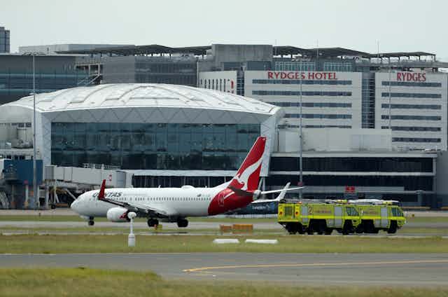 A Qantas plane sits on the tarmac with emergency vehicles nearby.