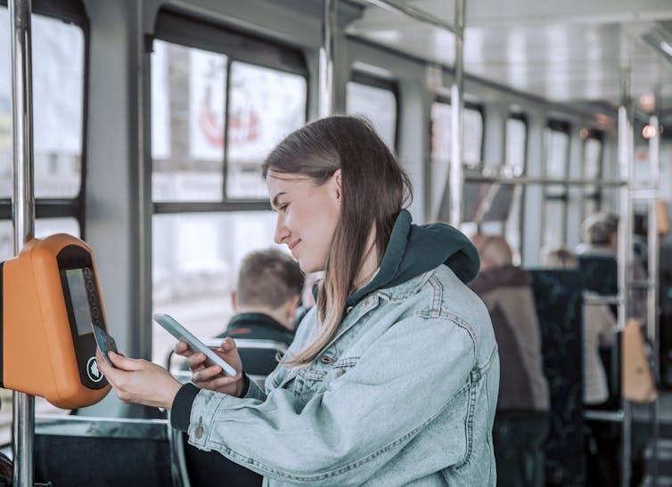 Woman holds phone as she uses a card to pay for her bus trip