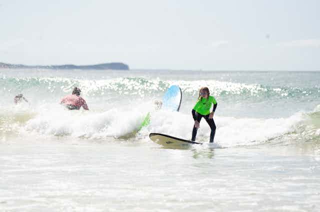 Teenagers surfing wearing wetsuit and t-shirt