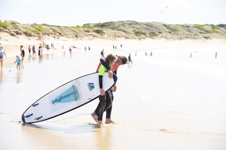 Ocean Mind participant holding surfboard with mentor on beach