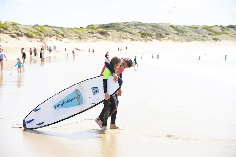 Ocean Mind participant holding surfboard with mentor on beach