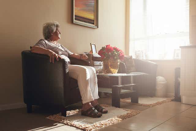 Older woman sitting alone in a room with an empty chair beside her