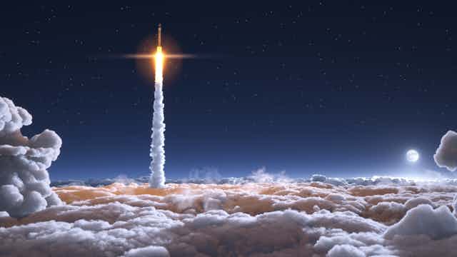 A rocket emerging through clouds at night producing a large plume of smoke.