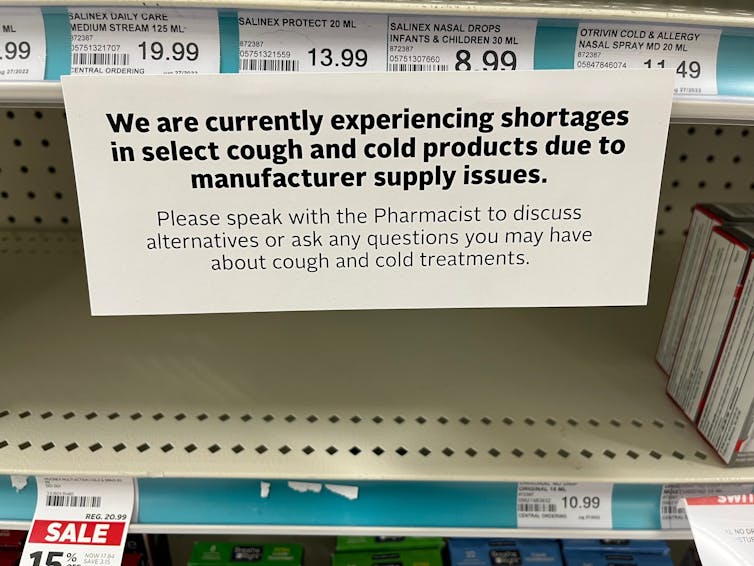 A photo of an empty pharmacy shelf, with a sign indicating supply chain issues have fuelled shortages of cold and flu medicines.