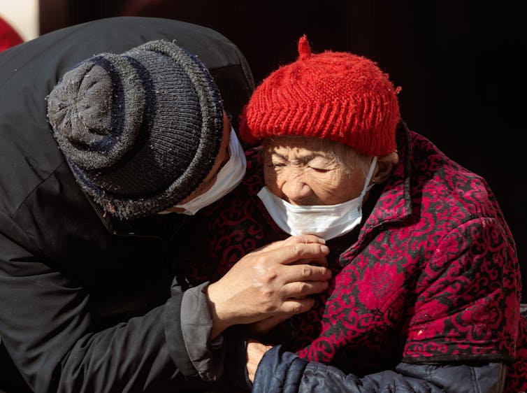 A Chinese man adjusts the mask on an elderly woman.