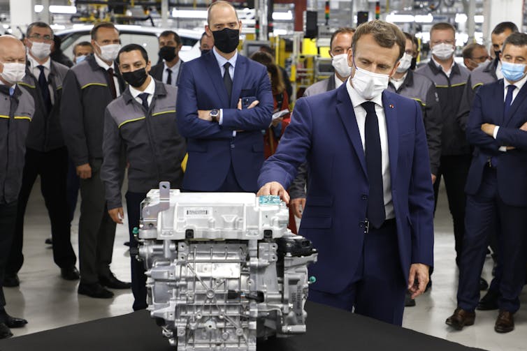 French President Emmanuel Macron inspects an EV battery in a factory.