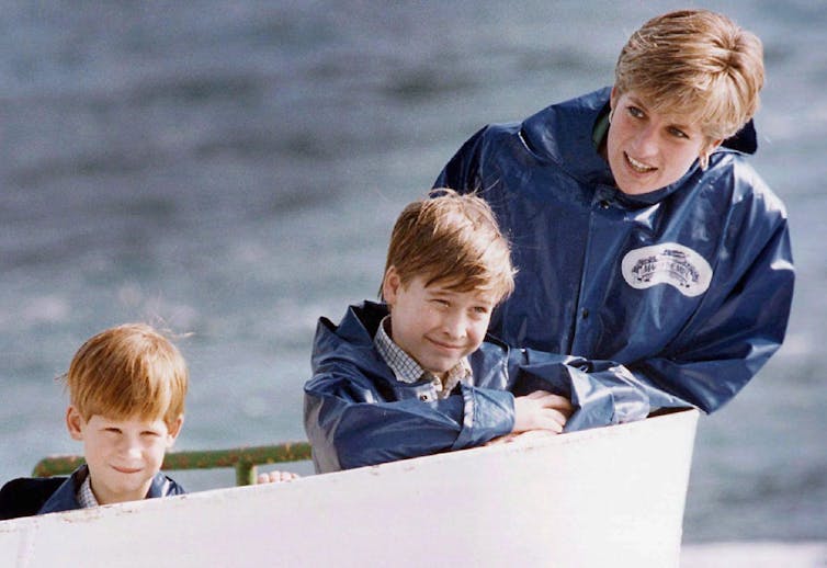 A woman with short blond hair smiles on a boat next to two young boys, one with red hair.