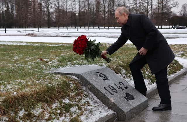 Vladimir Putin lays flowers on a memorial marked with the Soviet hammer and sickle and the year 1942.
