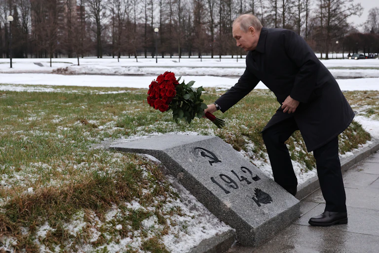 Vladimir Putin lays flowers on a memorial marked with the Soviet hammer and sickle and the year 1942.