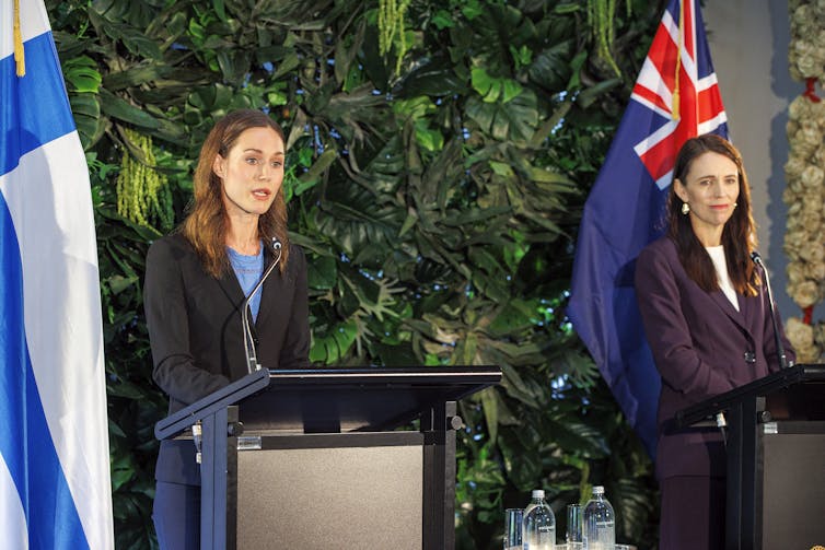 Two young white women wear formal clothing and appear at podiums.