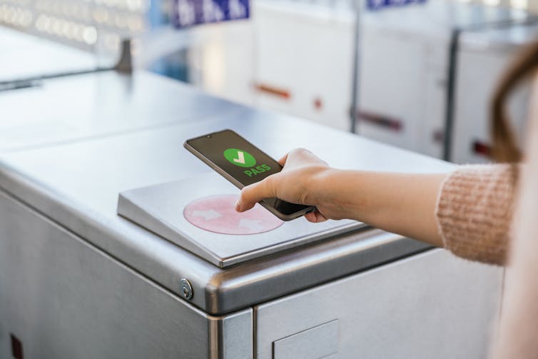 woman holds a phone to a reader at a train station ticketing barrier