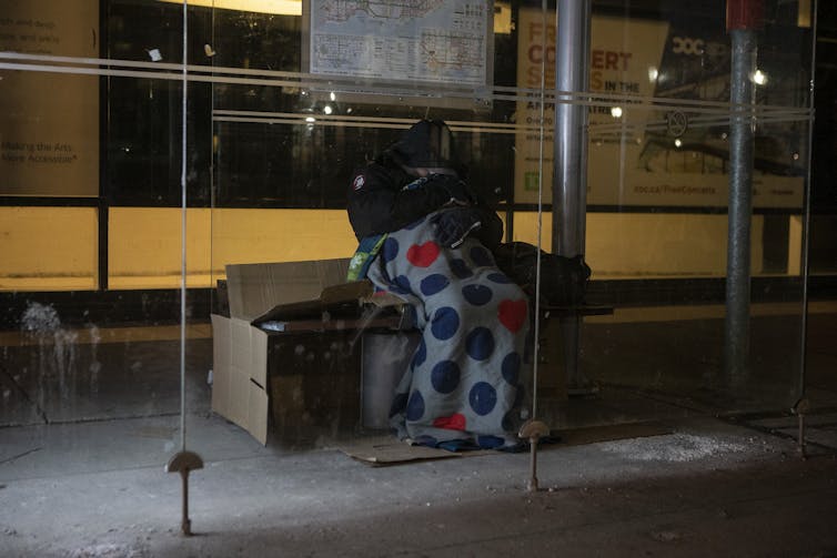 A homeless man sleeps in a bus shelter