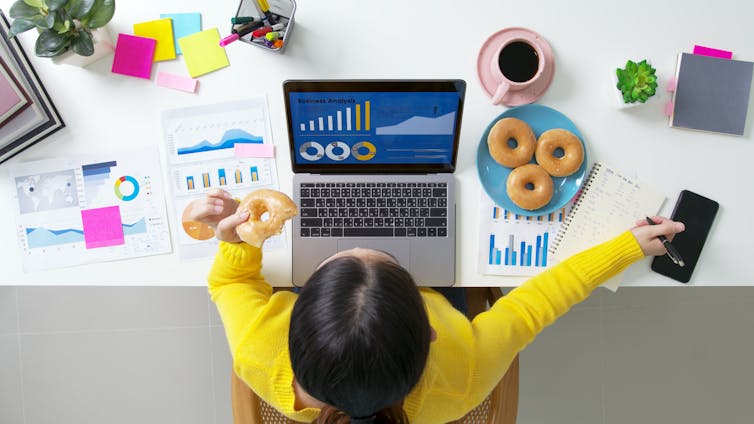 لقطة فوق رأس امرأة أمام جهاز كمبيوتر تأكل كعكًا.