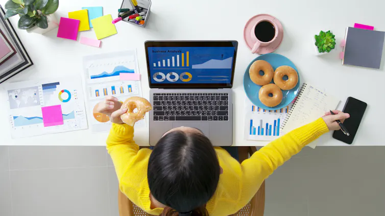 Overhead shot of a woman at a computer eating doughnuts.