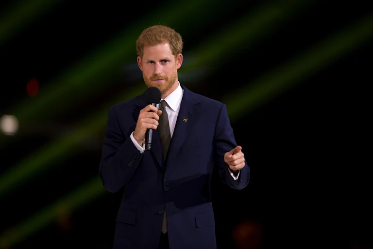 A man in a dark suit with a microphone against a dark background.
