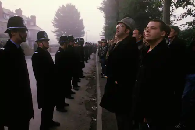 A line of police facing a line of striking miners on a foggy street in the 1980s.