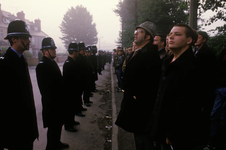 A line of police facing a line of striking miners on a foggy street in the 1980s.