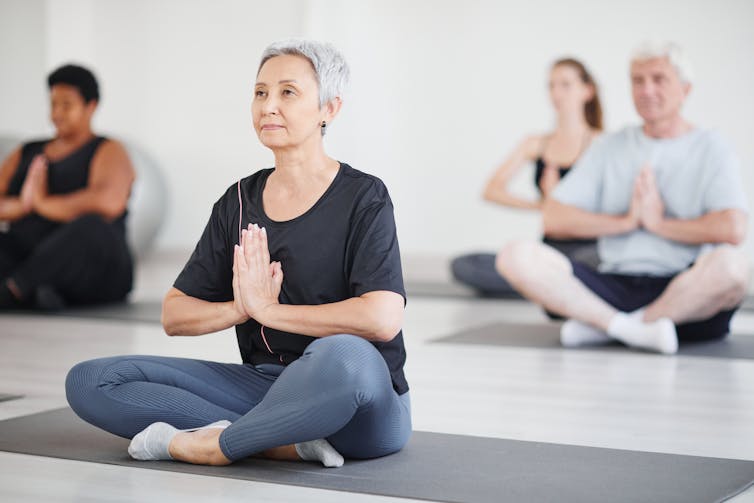 A group of people sitting on yoga mats with their hands folded in front of their chests.