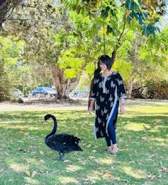 A woman in a dark salwar kameez dress standing next to a black swan on a grassy background