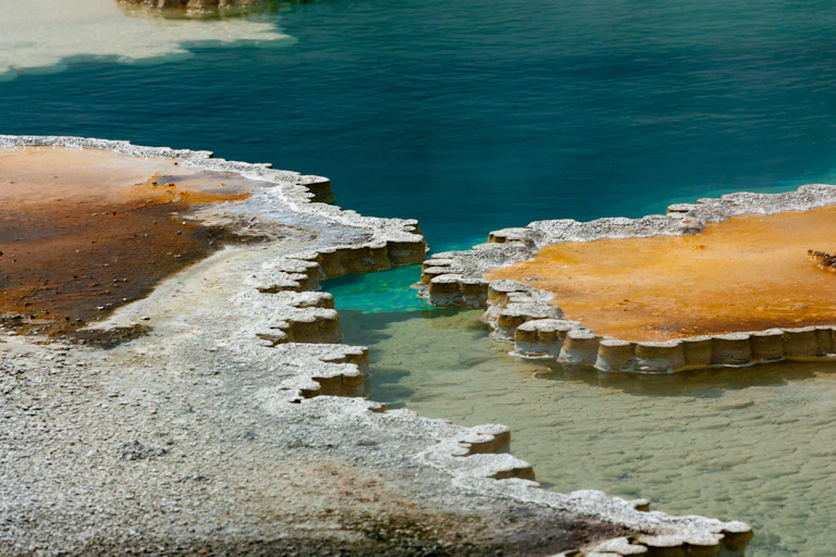 A deep cyan-blue pool with white silica deposits around the edge.