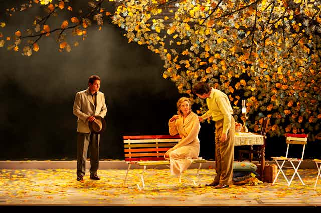 Three people on stage, under an autumn tree