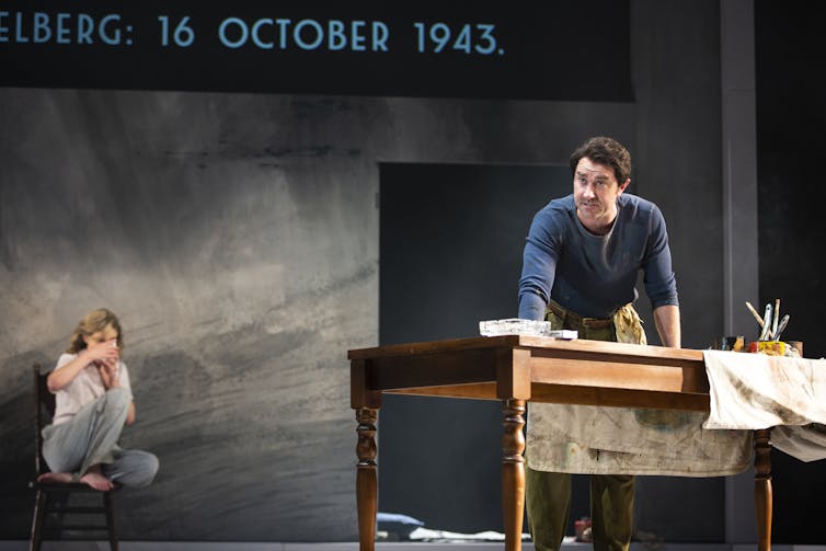 Two people on stage, a man leans over a painting table.