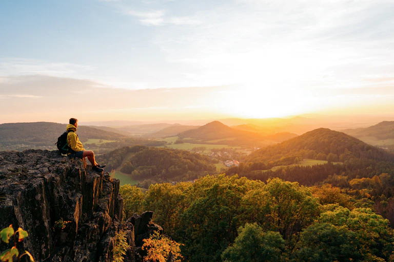A man sits on cliff and looks at forest
