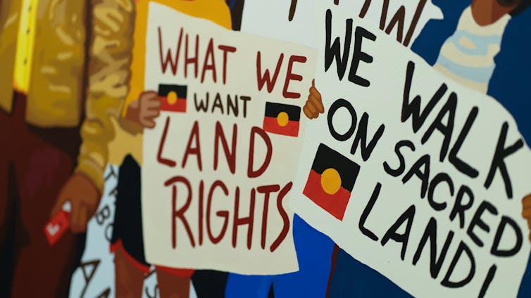 Painting: signs read 'we want land rights' and 'we walk on sacred land'