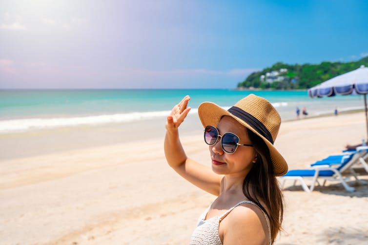 A woman protects her eyes from the sun on the beach.