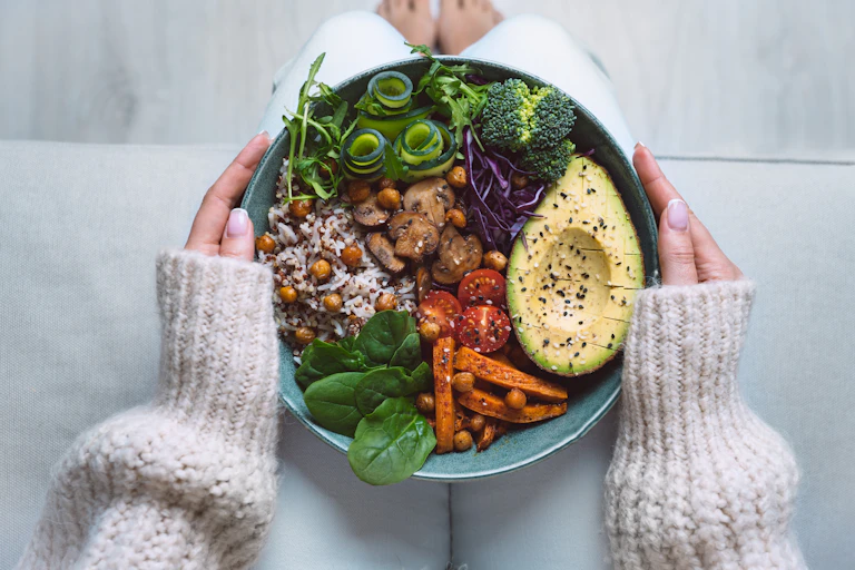 A woman holds a bowl of mixed vegetables on her lap.