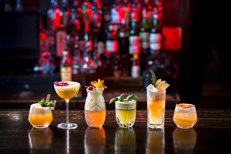 A series of cocktails in different glasses on a bar.